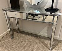 Full front view of the mirrored console table showing its single drawer with a crystal knob and mirrored legs.