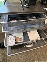 Photo of open metal mesh drawers showing assorted stationery, envelopes, clipboards, and paper items