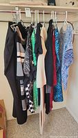 Nine women's clothing items on hangers including pants, dresses, and tops in various colors and patterns, some new with tags.