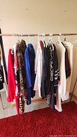 Wide view of various women's clothing items hanging on a wooden rack including dresses, tops, and jackets in various colors and patterns.