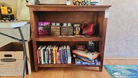 Front view of wooden horizontal bookcase with two shelves, holding books, puzzles, and various decor items.