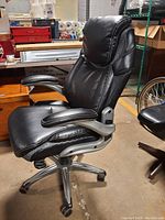 Side angle of the black leather rolling office chair showing padded seat, backrest, armrest and silver metal base with caster wheels.