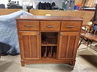 Front view of cherry wood buffet showing three drawers on top, two cabinet doors below, and three vertical cubbies in center for storage.