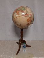 Full view of the 16-inch decorative floor globe mounted on a wooden tripod stand with a water bottle for size reference.