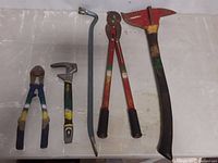 All firefighter tools including axe, bolt cutter, crowbar, branch lopper and FatMax Fubar laid side by side on white surface.