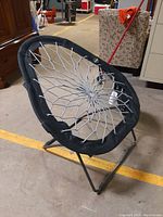 Pear-shaped foldable bungee chair by Bunjo with black metal frame and grey elastic cord seating, angled view.