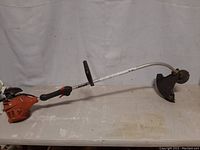Full side view of the entire Echo gas trimmer laid horizontally on a table showing curved guide shaft, handle, motor and cutting head with string trimmer.