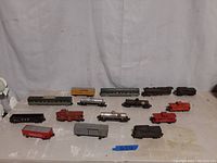 Overall lot of model train engine and cars arranged on a flat white surface showing all individual pieces in the lot.
