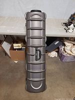Gray hard plastic golf club case, closed, showing ribbed exterior design and single handle on side.