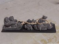 Side view of hand carved soapstone figurine showing Indigenous person on sled pulled by four dogs; placed on a concrete surface.