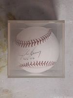 Front view of the baseball inside a clear acrylic display case, showing John Henry's signature and 'WS 04' inscription.