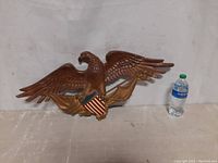 Front view of the metal American eagle wall plaque displayed next to a water bottle for size reference.