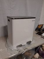 Front and angled side views of the white Songmics dual pedal trash can with branded logo visible and plastic wrap at base.