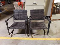 Front view of two dark brown polyethylene rattan rocking chairs showing woven seats, armrests, and rockers.