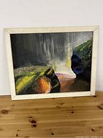 Framed landscape painting showing cliffs, greenery, and a stormy sky with atmospheric light effects.