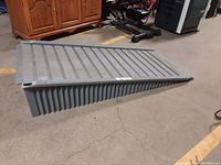 Side angle of sturdy gray poly ramp on concrete floor, showing approximate height and ramp incline