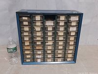 Front view of a blue metal organizer cabinet with 49 clear plastic drawers mostly filled with electronic diode components, one drawer missing, water bottle for scale.