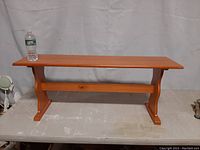 Small wood bench on a table with a water bottle for size reference, showing full front view of bench.