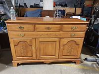 Front view of solid wood buffet showing three drawers with brass handles and three doors with floral painted accents.