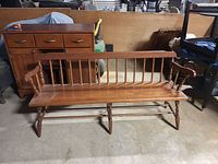 Full view of the antique wooden spindle back settle bench with visible scratches and armrests, showing its length and front design.