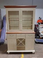 Front view of the wood hutch and buffet cabinet showing glass doors on top, drawers, cabinet doors, and wine rack below.