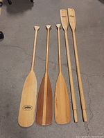 Full set of five wooden oars and paddles laid out together showing size and style differences.
