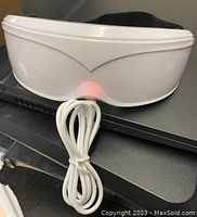 Front view of white plastic electric eye massager on table with attached USB cable coiled