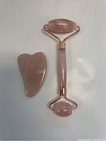 Pink jade facial roller and Gua Sha scraping tool on a white background, showing clear details of pink polished stone and rose gold framework on the roller.