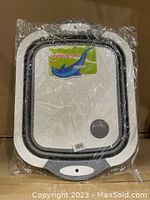 Photo of packaged foldable multifunction chopping board and colander in white and grey, showing front with cutting board surface and size label.