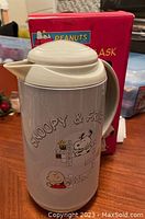 Front side of the grey vacuum flask showing Snoopy, Woodstock, Charlie Brown graphics and crossword-style text.