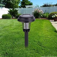 Solar bug zapper garden light stake shown outdoors installed in lawn with garden and fence background.