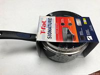 Top angle view of T-Fal Signature saucepan showing handle and packaging label indicating heat resistant and non-stick features.