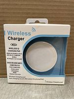 Front view of the retail box showing the white round wireless charger visible through a circular window. Box includes product information and branding 'Wellson Wireless Charger'.
