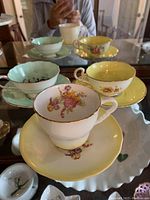 Three pastel colored teacups with matching saucers in yellow, green, and pink, displayed on a reflective surface