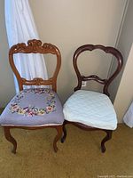 Pair of vintage style wooden frame chairs shown side by side, one with floral needlepoint upholstery and the other with cream quilted seat cover.