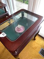 Glass top side table with mahogany-finish wood frame and visible glass door to display cabinet inside.