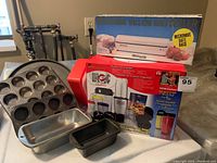 Photo showing Magic Bullet Deluxe 25-piece set box alongside Decosonic vacuum bag sealer box and various baking pans including muffin and loaf pans