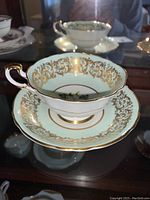 Close-up angle of Paragon Dogwood teacup on matching saucer with gold scrollwork and dogwood flower inside cup center.