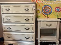 Full view of white highboy dresser and matching side table with floral wall background.