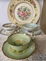 All three tea cup and saucer sets arranged on a white knit cloth with floral plate in background.
