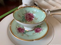 Photo of Old Royal teacup and saucer showing soft green interior with pink floral decal and gold rim, handle, and foot.