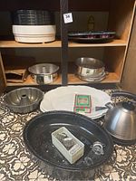 Overview of kitchen hardworker items showing roasting pan, turkey plates, food dehydrator trays, baking pans, and electric kettle on patterned surface.