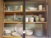 Front view of cabinet shelves with assorted glassware, Corelle dishes, mugs and bowls.