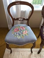 Front view of wooden chair with curved back and blue floral needlepoint upholstered seat.