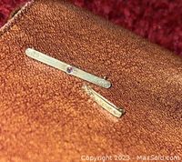 Two 10K men's pins placed on a brown textured surface showing details of the amethyst stone and gold markings.
