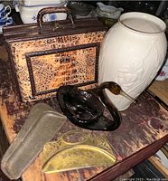 Brown art glass swan figurine, tall white Lenox vase with floral embossed pattern, two old crumb scrapers with metal blades, all displayed on wooden surface.
