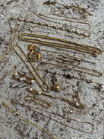 Multiple pieces of assorted gold-filled chains, earrings with pearls and stones, pendants including heart-shaped and ribbon designs, laid out flat on a carpet.