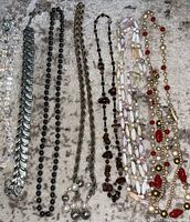 Photo showing seven assorted necklaces, varying styles including metal linked, hematite beads, silver chain with beads, brown stones, multi-strand beads, and pearl with red bead necklaces