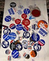 Photo showing assorted political pins spread on a surface, featuring candidate names like Dob Butera, Schulze, Thornburgh Scranton, and others.