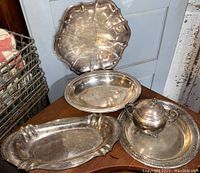 Four silver plate serving pieces including sugar bowl on perforated tray and three trays with visible wear.